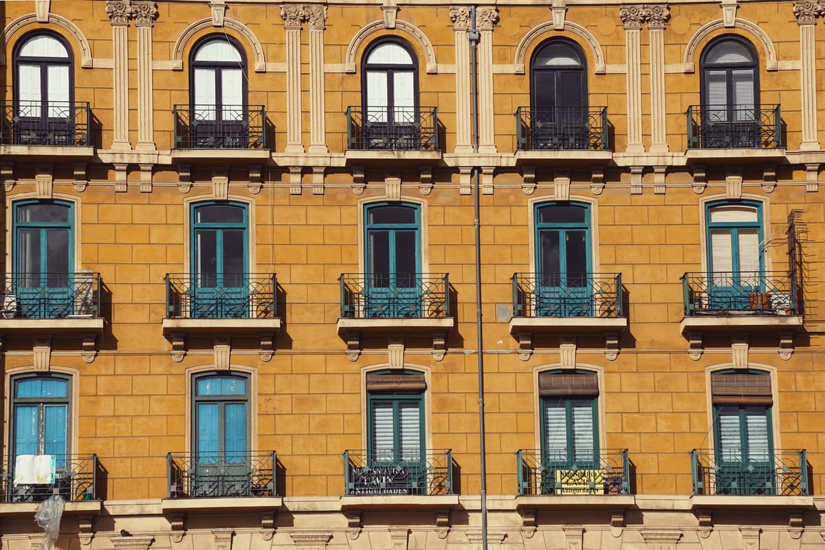 Fachada de varias plantas pintada en ocre, con ventanas de contraventanas verdes, balcones de hierro y molduras en un tono más claro.
