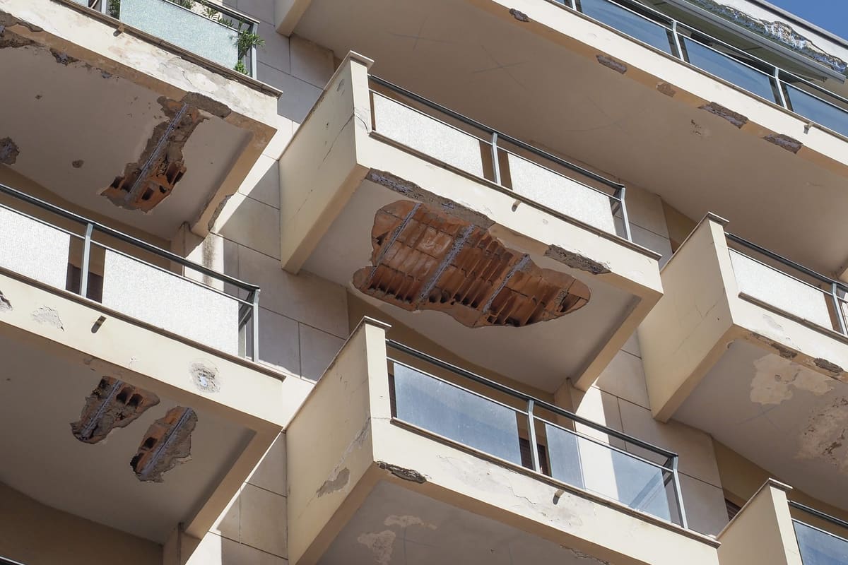 Balcones de un edificio de viviendas vistos desde abajo, con el revestimiento caído y las viguetas oxidadas del forjado a la vista, y desconchones en los cantos.